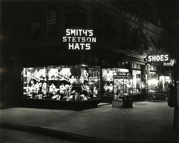 Lit up store fronts advertising Smiths Stetson Hats, Shoes, Liquors, c