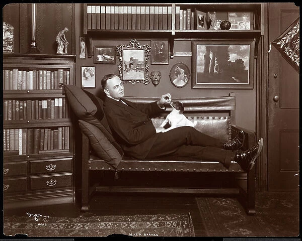 Will R. Barnes reclined on a couch with a dog in his library  /  studio