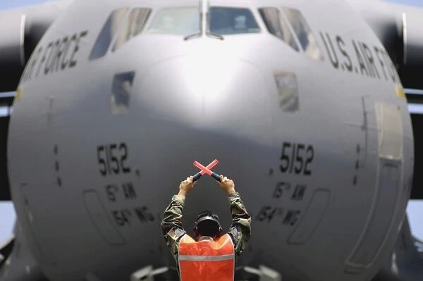 Ground crewmember marshals a C-17 Globemaster III to its parking spot