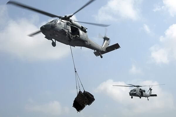 Two MH-60S Sea Hawk helicopters transfer cargo during a vertical replenishment