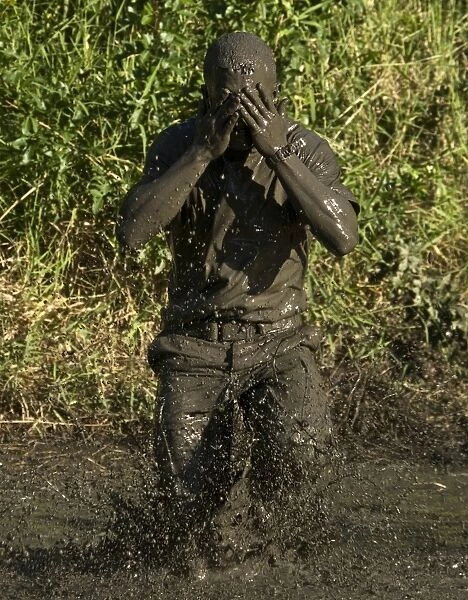 A participant wipes mud from his face after jumping in a pond