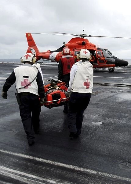 Personnel carry an injured sailor to a coast guard MH-65 Dolphin helicopter