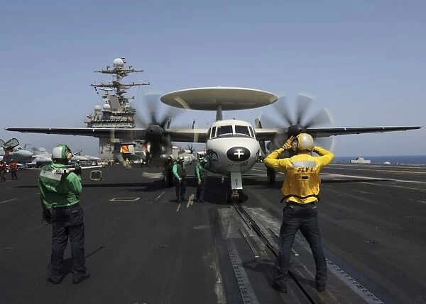 A plane director guides an E-2C Hawkeye onto the catapult for launch