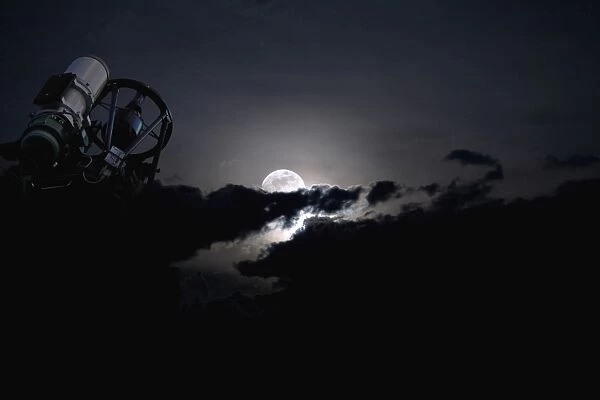 Telescope pointed out to the night sky with moon and clouds