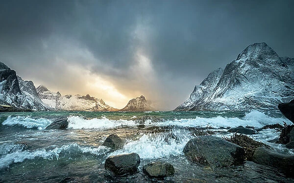 Winter storm clouds gathering along rocky shore surrounded by snow-covered mountains, Lofoten Island, Norway. March, 2023