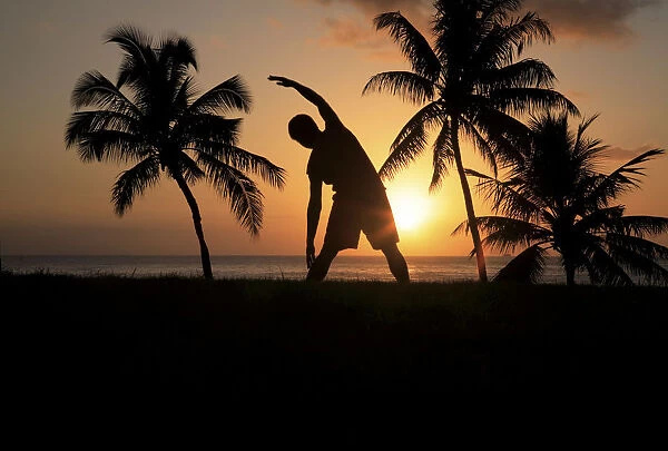Hawaii, Oahu, Silhouette Of Man Stretching Near The Beach As The Golden Sunsets
