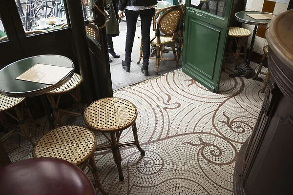 Looking Down At The Floor Of A Parisian Cafe With Small Square Tiles, Traditional Tables And Stools, And The Wooden Bar; Paris, France