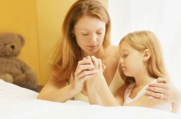 Mother And Daughter Praying Together Beside Bed