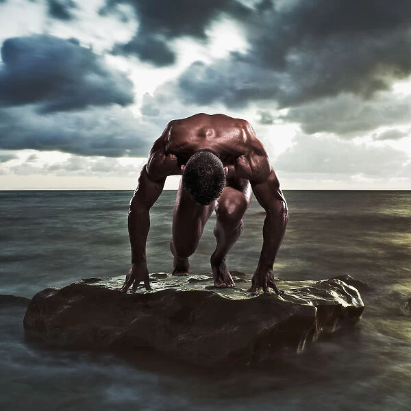 A muscular man in the starting position on a wet rock in the water; Tarifa cadiz andalusia spain