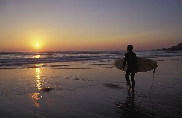 Silhouetted Surfer On Sandy Beach At Sunset