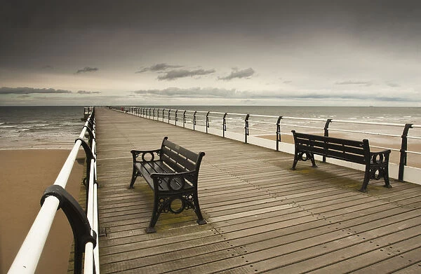 A Wooden Pier With Benches Looking Out Over The Beach And Water; Saltburn Cleveland England