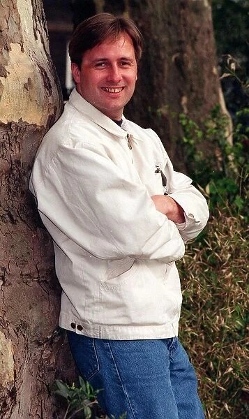Actor Gary Webster leaning against tree arms folded white jacket and jeans April 1997