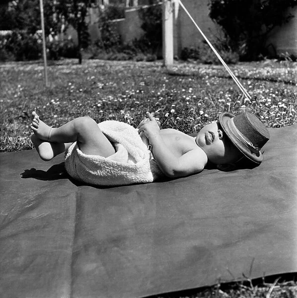 Baby having a sleep on a rug wearing nappy and hat. June 1950 O24582