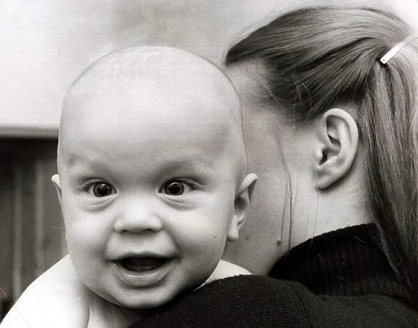 A cute baby looking over shoulder of his mother February 1979