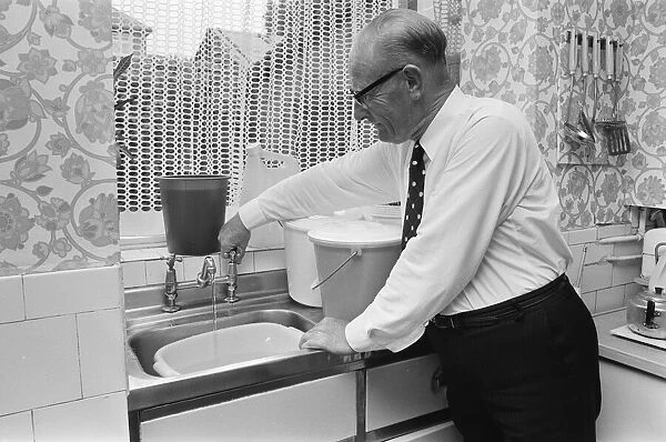 An elderly man running the tap in his kitchen, filling up buckets as a water shortage