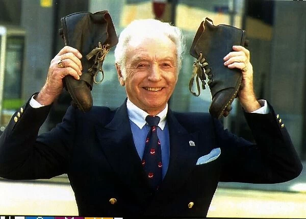 Football legend Sir Stanley Matthews holds up a pair of old fashion football boots in