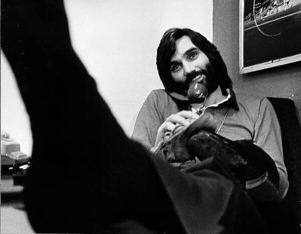 George Best in his office cleaning his shoes whilst chatting on the phone May 1974