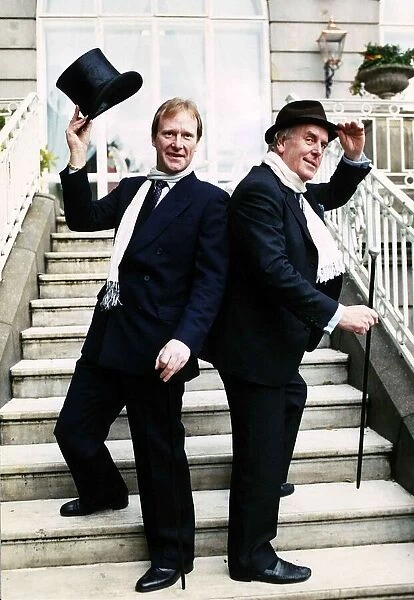 George Cole actor and Dennis Waterman standing on doorsteps raising a top hat and cane