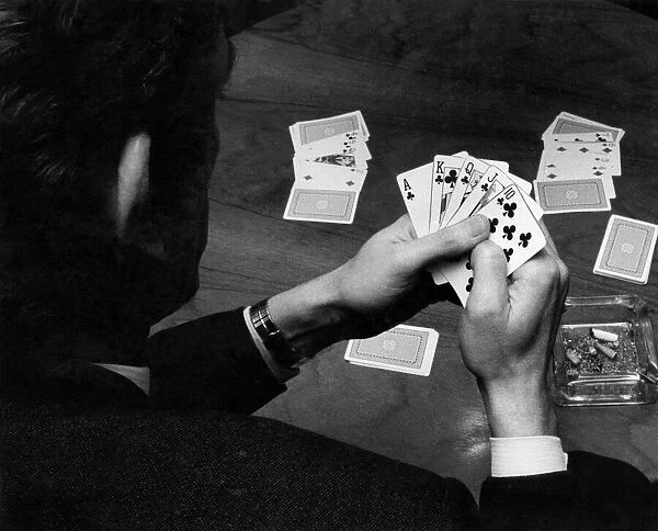 A man holding his hand of cards, a royal flush, while playing poker. February 1972