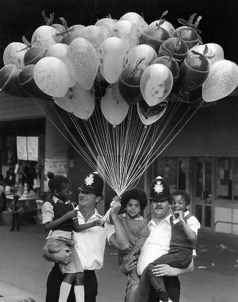 Two policemen holding three young boys in their arms with lots of toy Balloons