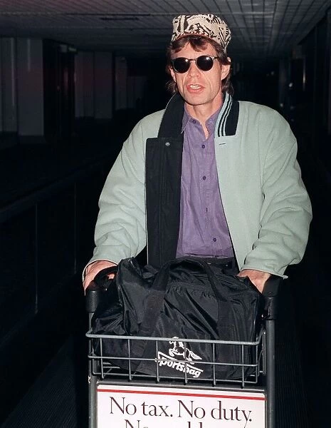 Rolling Stones: Mick Jagger arriving at Heathrow airport pushing trolley in February 1990