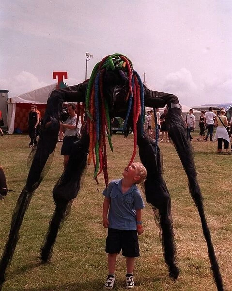 Stilted figure towering over a small boy at T in the Park wearing a bright coloured wig