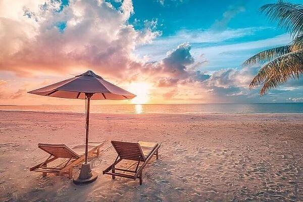 Beautiful tropical sunset scenery, two sun beds, loungers, umbrella under palm tree. White sand, sea view with horizon, colorful twilight sky calmness