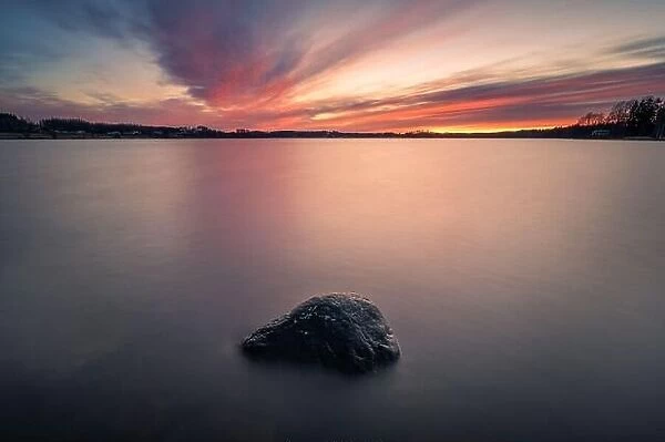 Scenic sunset with peaceful lake and rock at spring evening in Finland