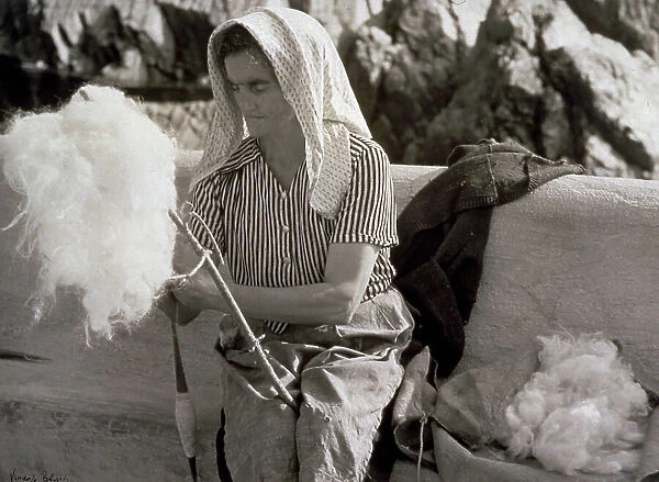 Elderly lady in humble attire shown spinning wool
