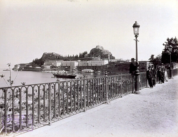 The fortress of Corfu with a stretch of coast. In the foreground an iron balustrade and a street lamp. A few children on the ocean boulevard
