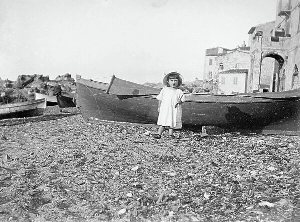 A little girl posing in front of a boat by the sea