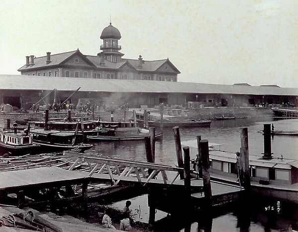 The port warehouses of Yokohama in Japan. In the foreground a gangway. On the river barges are moored