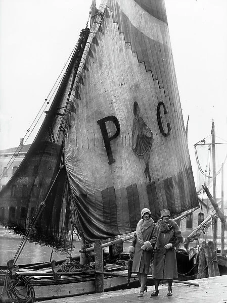 Portrait of two young women posing in front of a sailboat in the port of Chioggia