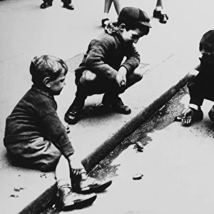 Three boys playing marbles in the gutter