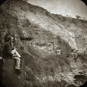 A man sitting on a stone block next to a low cliff face