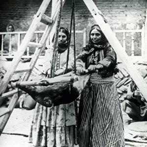 Two Persian women rocking a goatskin to churn milk