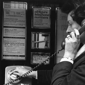Woman dialling 999 in a public telephone box, London