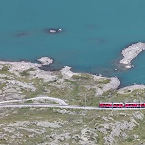 The Bernina Express train passes on the shores of Lago Bianco, Bernina Pass, Canton of Graubunden