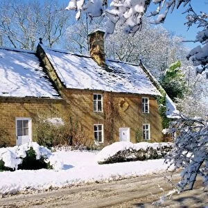 Cotswold farmhouse beside a road covered in snow in winter in England