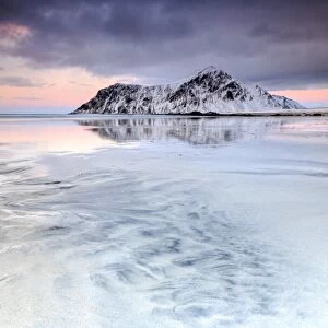 Sunset on Skagsanden beach surrounded by snow covered mountains reflected in the cold sea