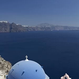 White church with blue dome and pink belltower overlooking the Caldera, Oia, Santorini