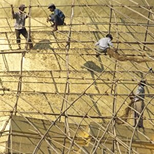 Workers on bamboo scaffolding applying fresh gold leaf to the Shwedagon Pagoda