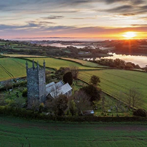 Aerial view of sunrise over the Church of St Laudus in the parish of Mabe near Falmouth, Cornwall, England. Spring (May) 2023