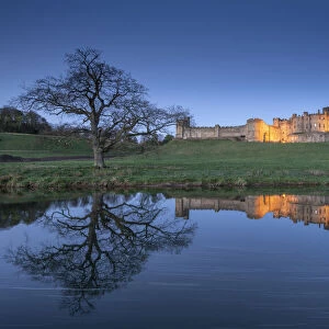 Alnwick Castle illuminated at twilight and reflected in the River Aln, Northumberland