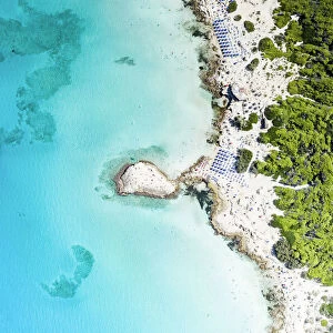 Beach umbrellas on sand beach and cliffs by turquoise sea from above, Punta della Suina