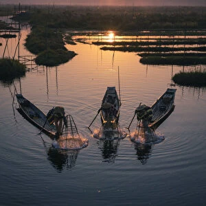 Three fishermen catching fish from boats using traditional conical nets at sunrise