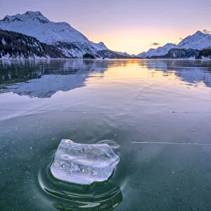 Ice block on frozen water of Lake Sils lit by a cold winter sunset, Graubunden, Engadine