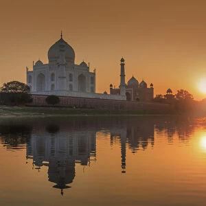 India, woman crossing the Yamuna river on a camel with the Taj Mahal reflecting in
