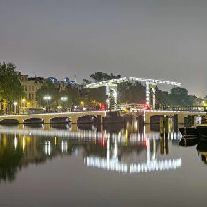 Magere Brug over the river Amstel illuminated at night on foggy evening, Amsterdam