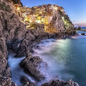 Manarola village illuminated by the blue light of dusk with its typical pastel colored houses